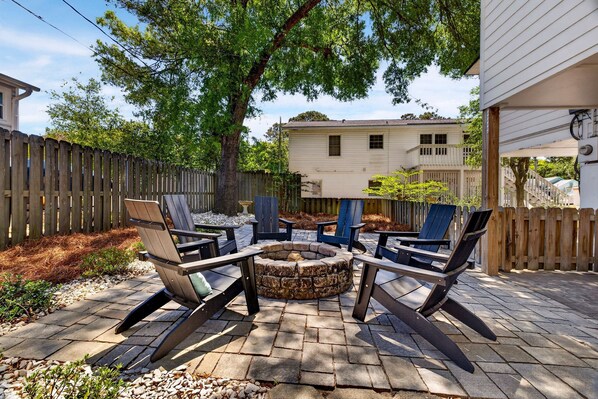 A patio with a stone fire pit and Adirondack chairs.