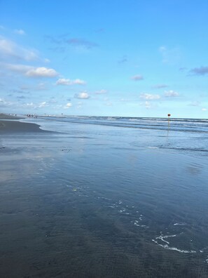 A beach with a clear sky, waves, and a lifeguard flag.