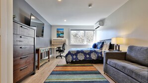 A bedroom with a bed, a desk, a chair, a dresser, a TV, and a window. - Swirl Suite Annex: Studio w/ Kitchenette and Workspace. Discounted Ski Rentals. (Killington)