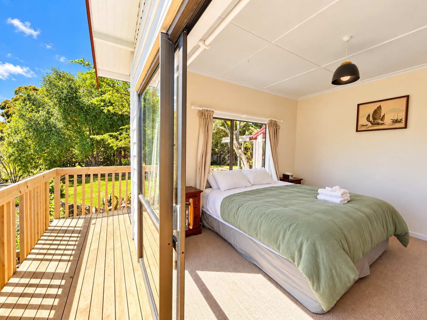 A bedroom with a bed, a nightstand, a window with curtains, a ceiling light, and a view of a garden.