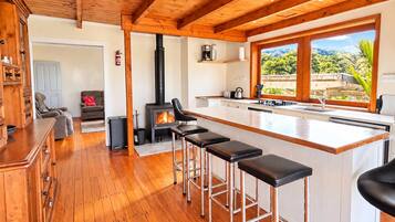 A modern kitchen with a central island, wooden flooring, and a large window offering a view of greenery.