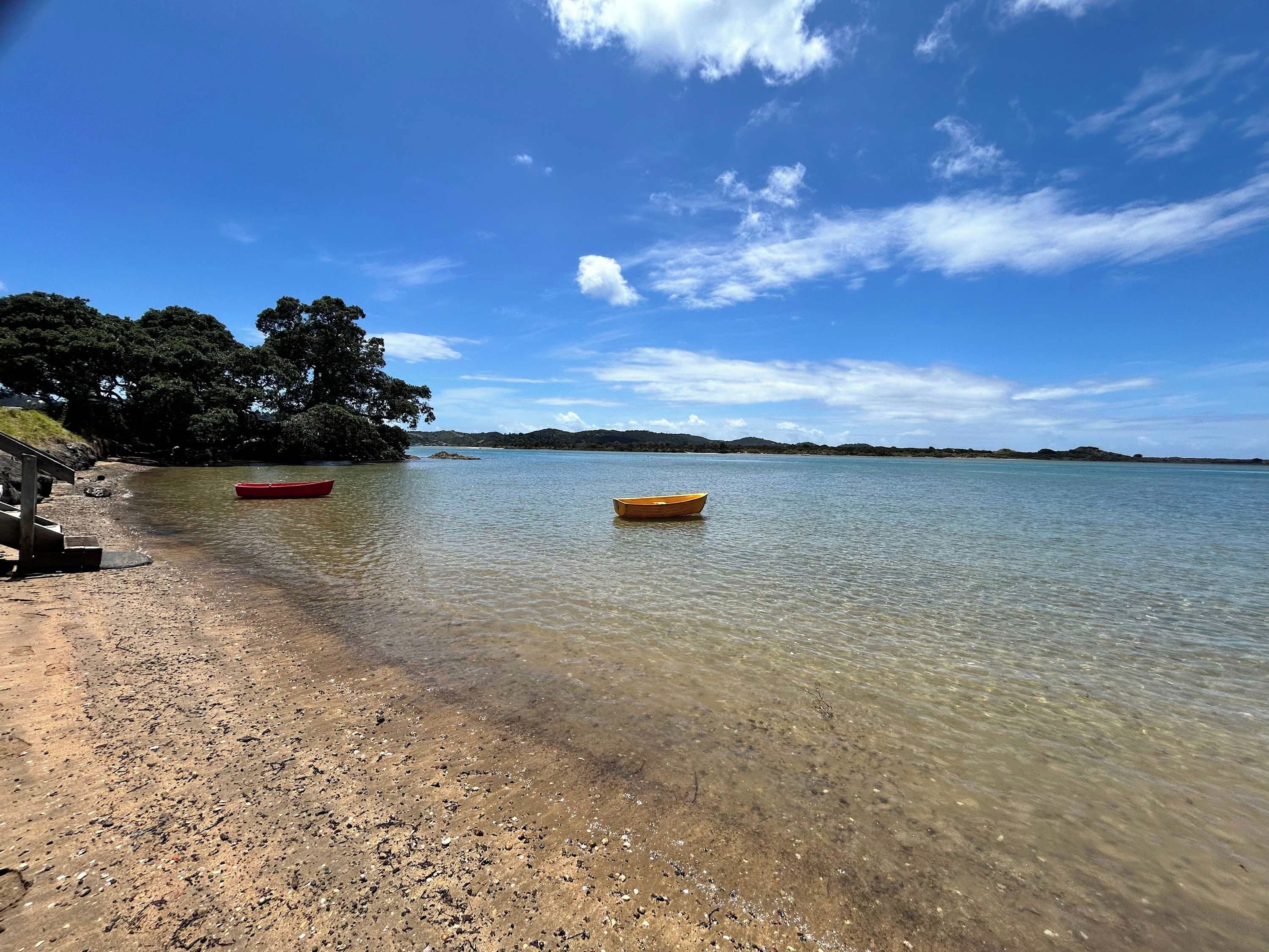 A clear beach with two boats, a rocky shoreline, and a forested area in the background.