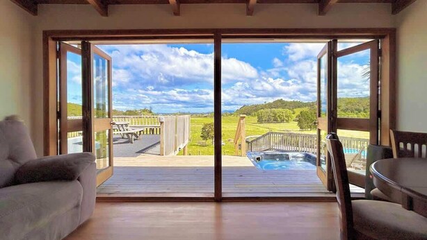 Ein Zimmer mit einer großen Schiebeglastür, die auf eine Terrasse mit Whirlpool und Blick auf eine grüne Landschaft führt.