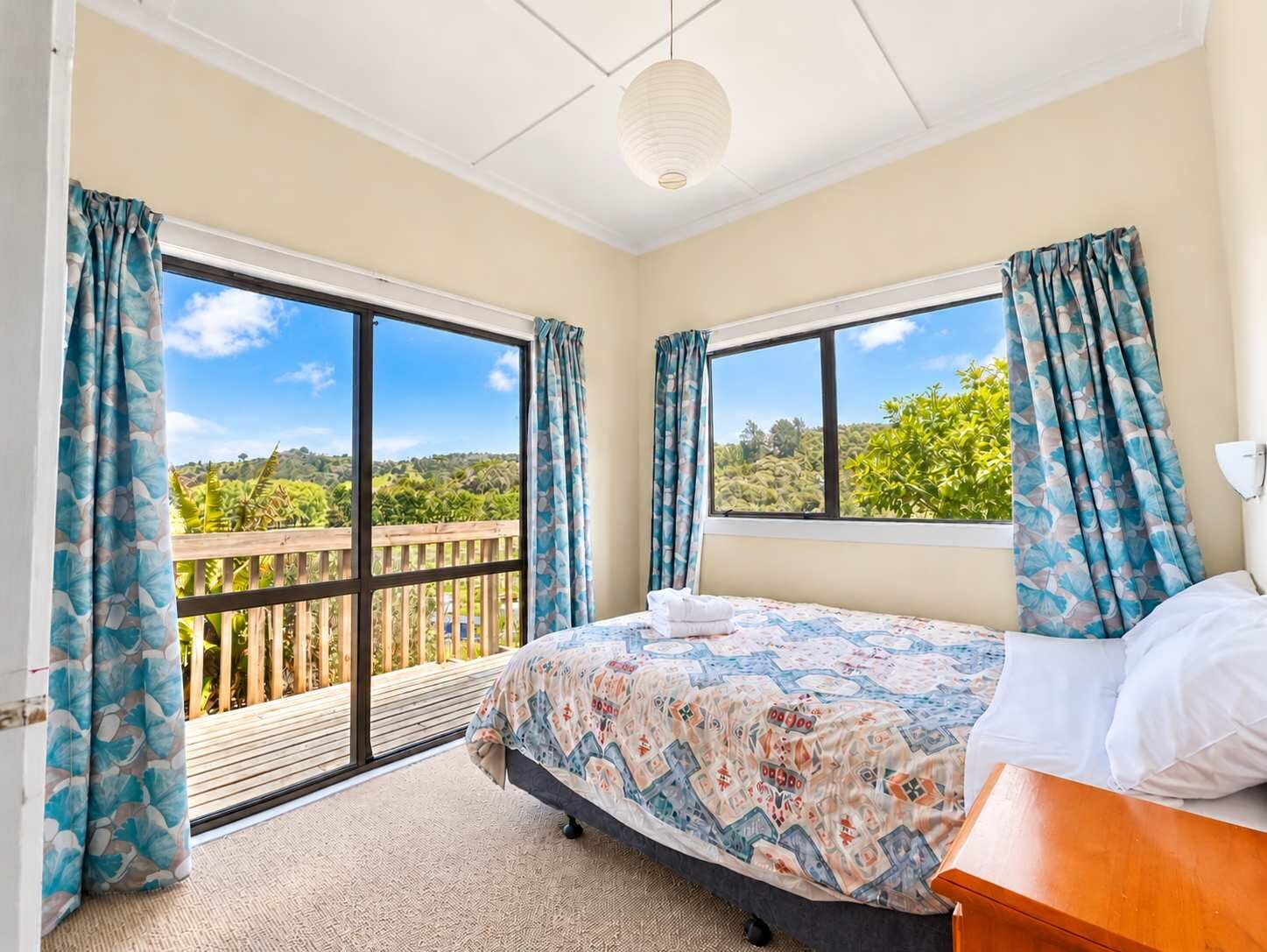 A bedroom with a bed, a wooden nightstand, and a view of a balcony with a wooden railing.