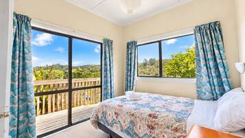 A bedroom with a bed, a wooden nightstand, and a view of a balcony with a wooden railing.