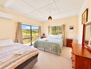 A hotel room with two beds, a wooden dresser, a nightstand, a ceiling light, and a view of the outdoors. - Ngunguru Lodge - Holiday HQ (Ngunguru)