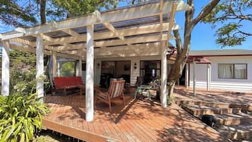 Uma área externa coberta com deck de madeira, um banco vermelho e uma mesa com cadeiras.