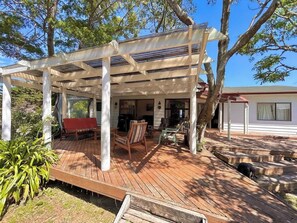 Un espacio al aire libre cubierto con piso de madera, un banco rojo y una mesa con sillas.