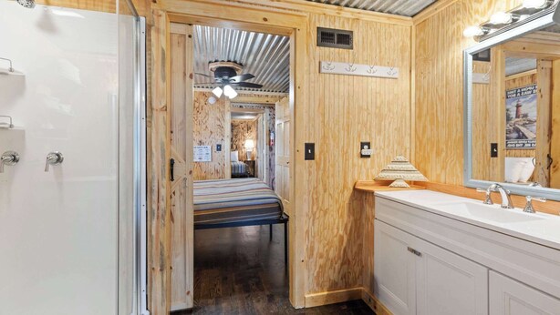 Un intérieur en bois avec un lit, un lavabo blanc et un miroir.
