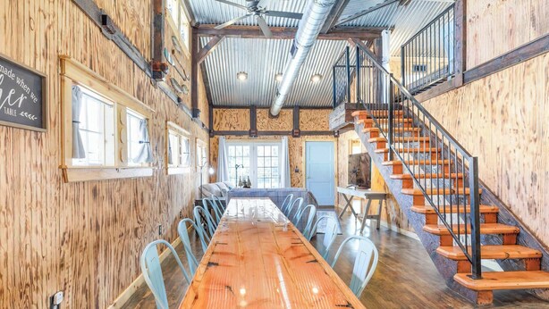 Un comedor amplio con una larga mesa de madera, sillas de metal y una escalera con escalones de madera.