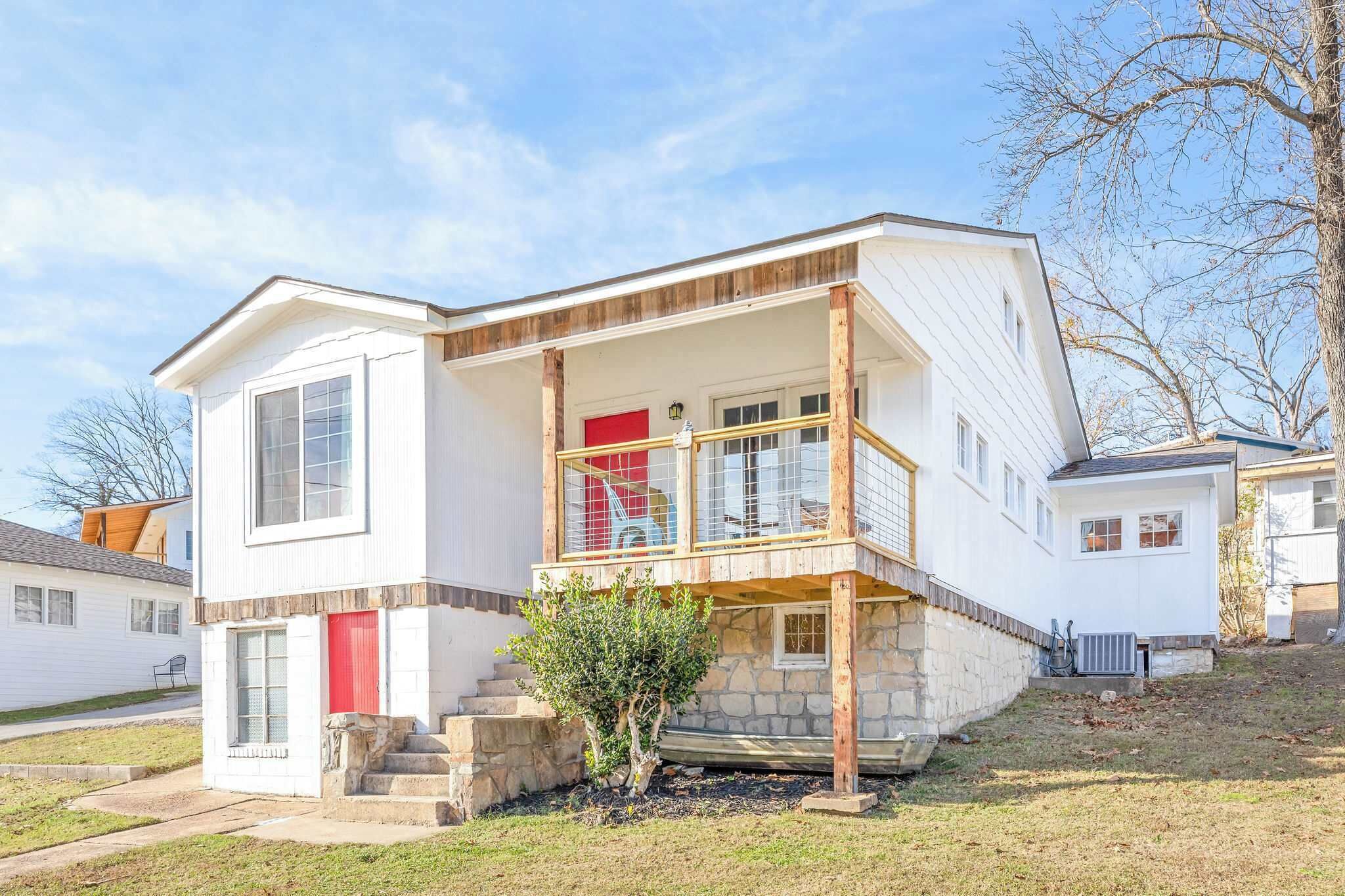 A two-story house with a front porch, a red door, and a small tree in front.