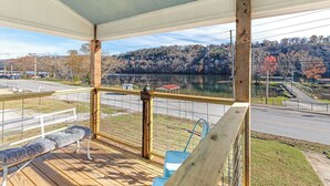 Una terraza cubierta con un banco, barandilla y vista a un lago y una carretera.