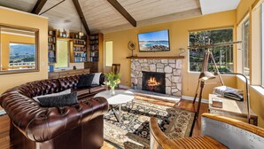 A cozy living room with a stone fireplace, leather sofa, and a large TV. - 3959 Hedgehog - Walk to Town and Beach, Ocean View (Carmel)