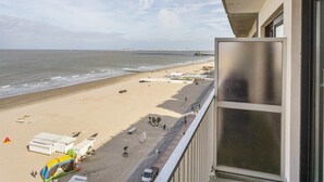 A beach view from a balcony with a clear sky, sandy beach, and a few beach umbrellas. - Studio in Blankenberge With Sea Views (Blankenberge)