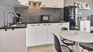 A modern kitchen with white cabinets, a black countertop, a built-in microwave, and a black refrigerator. There is a dining table with chairs and a vase with flowers. - Studio in Blankenberge With Sea Views (Blankenberge)