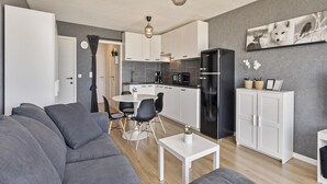A modern living room with a grey sofa, a dining table with chairs, a kitchen with white cabinets, a black refrigerator, and a hanging light fixture. - Studio in Blankenberge With Sea Views (Blankenberge)