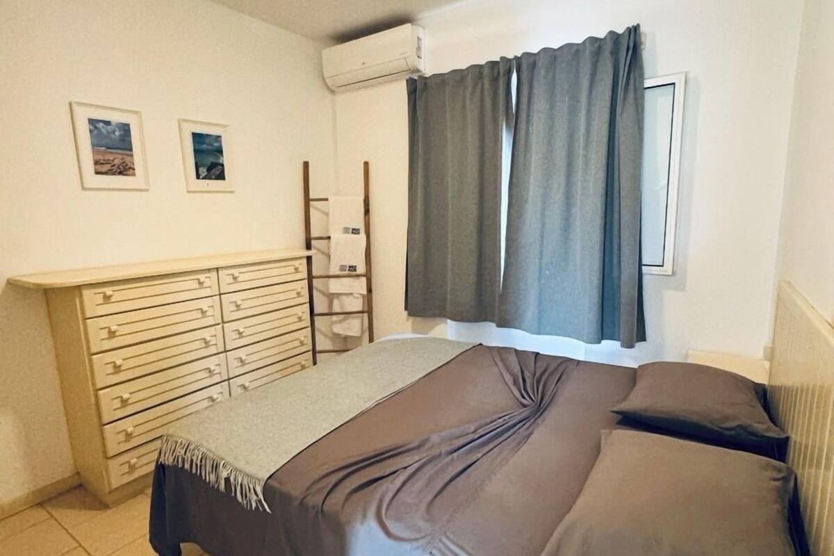 A bedroom with a bed, a dresser, a radiator, and an air conditioning unit.