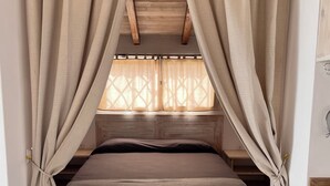 A cozy room with a bed, wooden ceiling beams, and beige curtains. - Wave Maze (Maio)