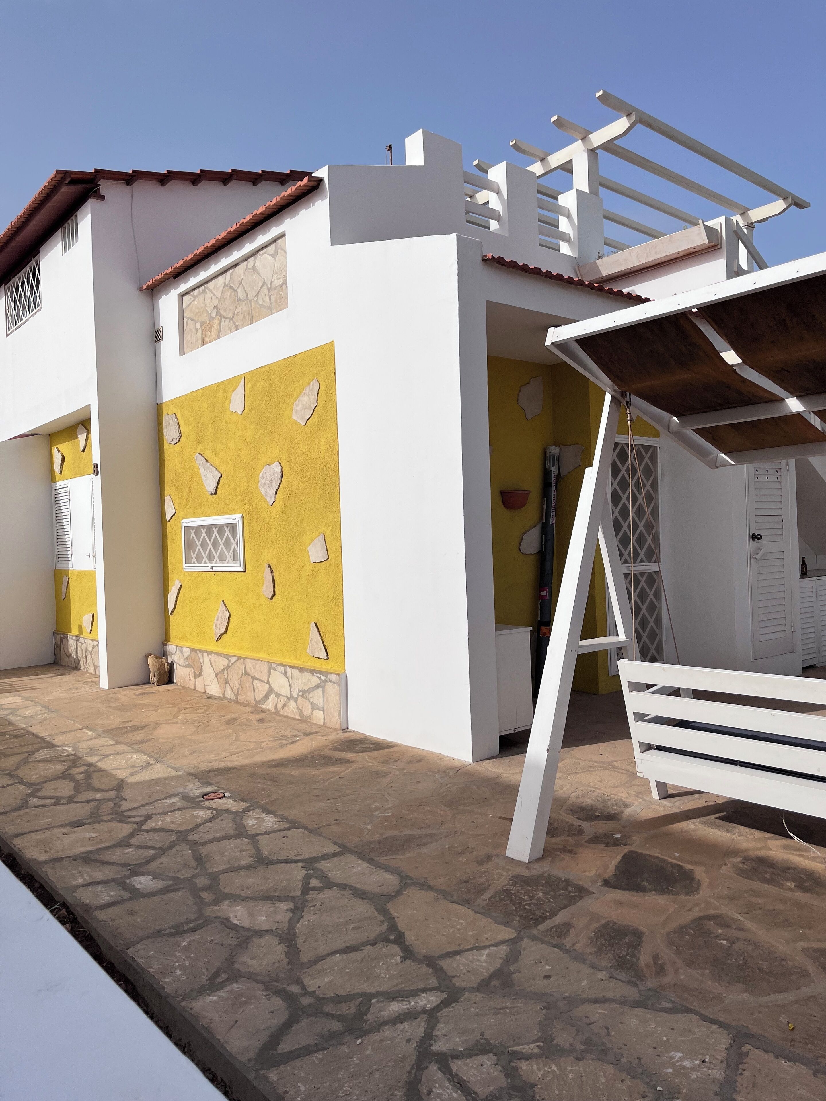 Un bâtiment à deux étages, doté d’une façade jaune et blanche, de détails en pierre et d’un espace extérieur abrité avec un banc.