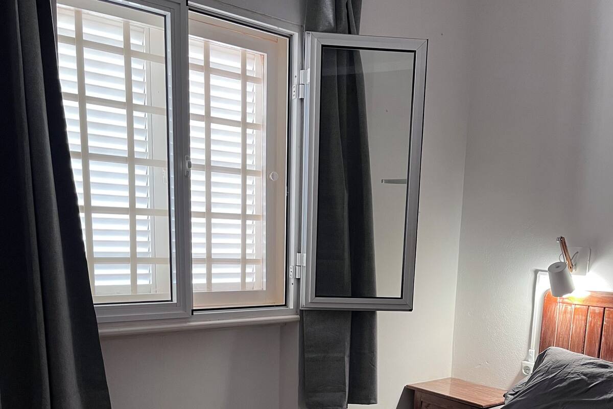 A bedroom with a bed, a nightstand, a lamp, and a window with curtains.