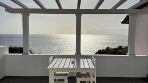 A covered patio with a white table and chairs, overlooking a body of water. - Wave Maze (Maio)