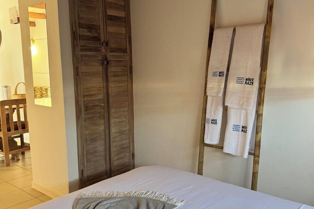 A hotel room with a bed, a wooden wardrobe, and a towel rack with towels.