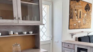 A kitchen with wooden cabinets, a glass-fronted upper cabinet, and a painting on the wall. - Wave Maze (Maio)