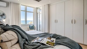 A bedroom with a bed, a window with curtains, a chair, and a wardrobe. - Apartment w Sea Views by Camps Bay Beach Kyanos (Cape Town)