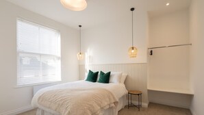 Ein Schlafzimmer mit einem großen Bett, einem kleinen Hocker, einer Heizung und einem Fenster mit Jalousien.
