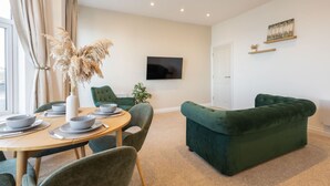 Ein modernes Wohnzimmer mit einem grünen Sofa, einem Esstisch mit Stühlen und einem an der Wand befestigten Flachbildfernseher.