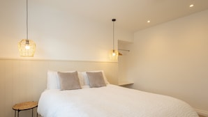 A neatly made bed with a white duvet and two pillows, a small round stool, and two hanging light fixtures. - Host Stay Apartment 4 King s Court (Scarborough)
