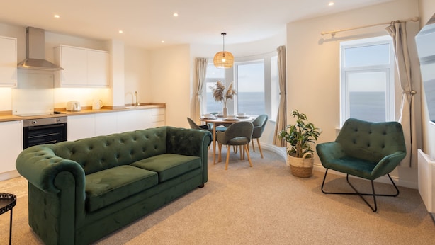 A modern living room with a green sofa, a dining area with a table and chairs, and a kitchen in the background. - Host Stay Apartment 4 King s Court (Scarborough)