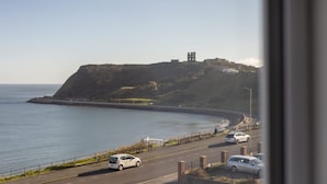 A coastal road with a white car parked on the side, a cliff with a tower, and a clear sky. - Host Stay Apartment 4 King s Court (Scarborough)