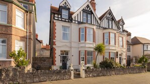 A row of Victorian-style townhouses with bay windows, stone walls, and a cobblestone street. - Host Stay The Keep (Llandudno)