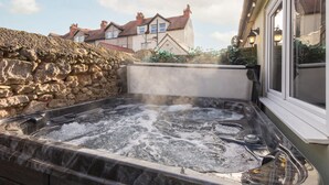 A hot tub with a stone wall backdrop and a house in the background. - Host Stay The Keep (Llandudno)