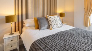 A neatly made bed with a patterned blanket, two bedside lamps, and a striped headboard. - Host Stay The Keep (Llandudno)