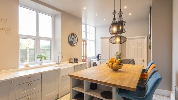 A modern kitchen with a wooden dining table, blue chairs, and a fruit bowl. - Host Stay The Keep (Llandudno)