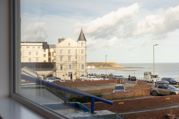 A hotel with a prominent tower, a parking area with several cars, and a view of the sea. - Host Stay Apartment 2 King s Court (Scarborough)