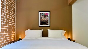 A hotel room with a brick wall, a framed picture on the wall, a large bed with white linens, and two bedside lamps.