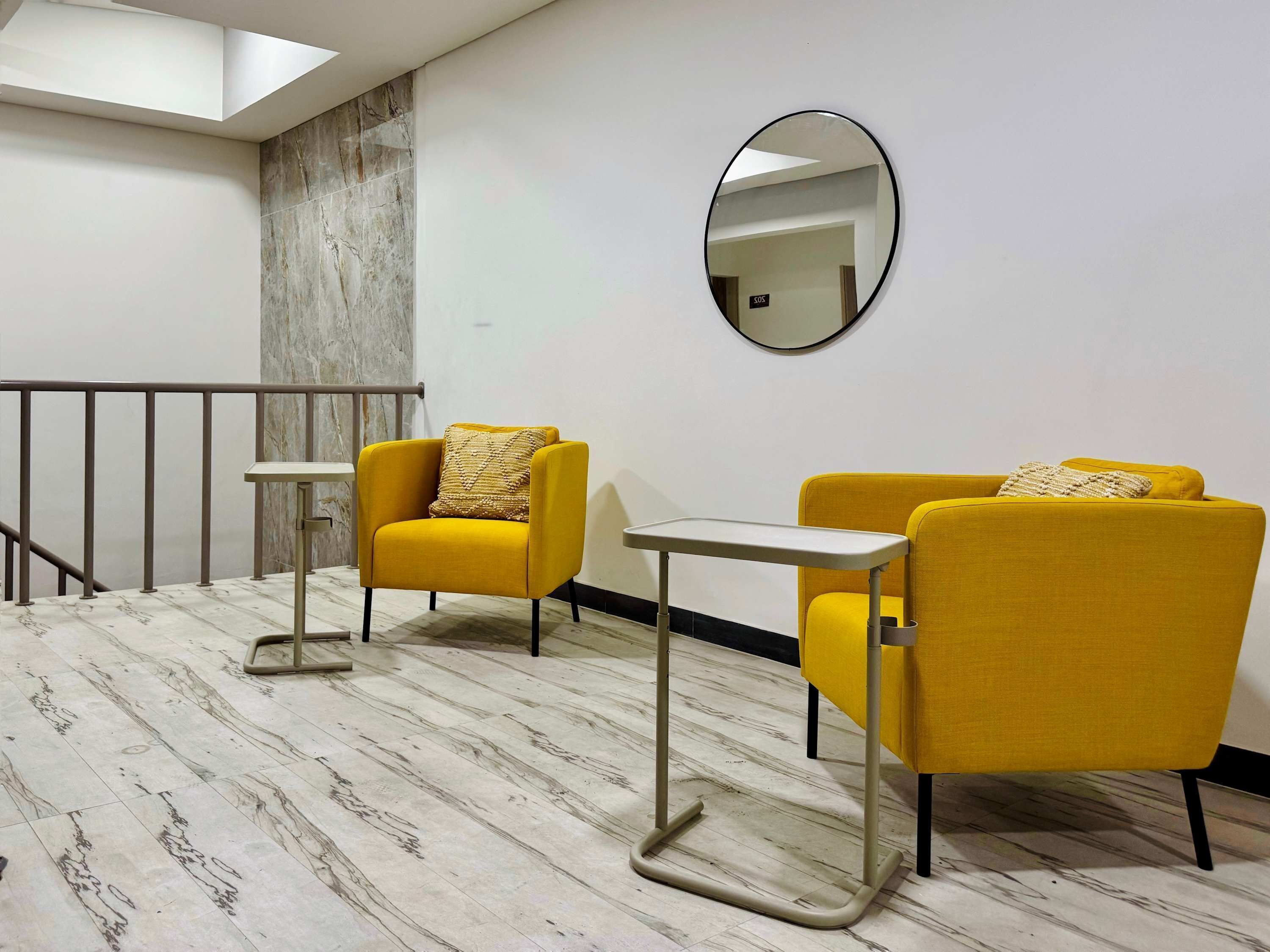 Ein modernes Hotelzimmer mit Marmorboden, zwei gelben Sessel, einem kleinen Tisch, einem runden Spiegel und einer Treppe mit Metallgeländer.
