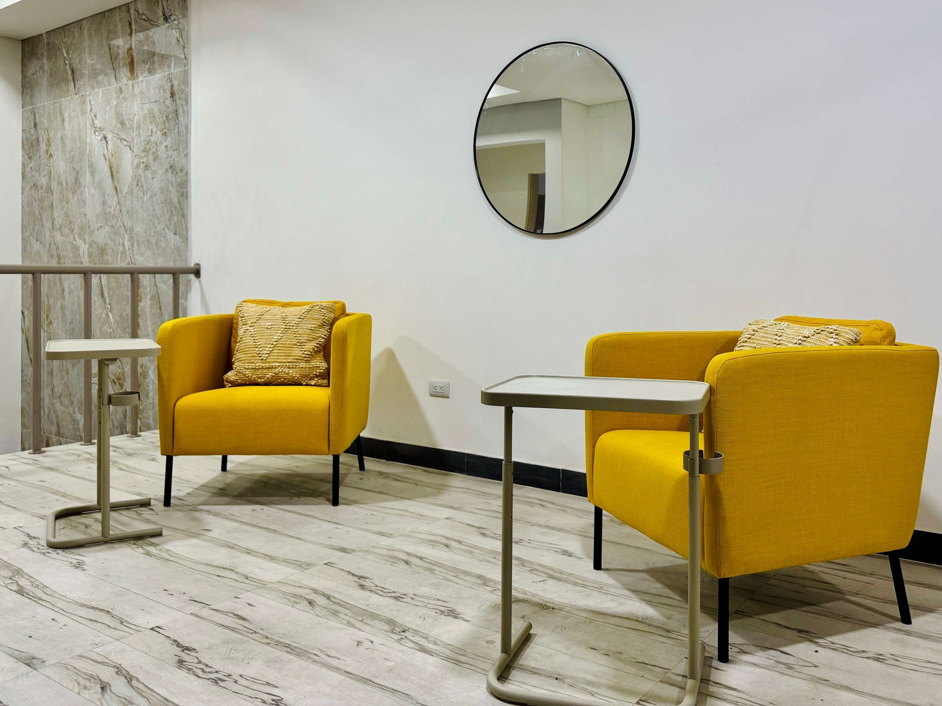 A room with two yellow armchairs, a small white table, and a mirror on the wall.