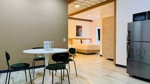 Ein Hotelzimmer mit einem runden Esstisch, vier Stühlen, einem Kühlschrank und einem Bett mit einem Nachttisch.