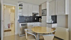 A modern kitchen with white cabinets, a stainless steel dishwasher, a microwave, and a round dining table with two chairs. - Apartment in Blankenberge With Sea Views (Blankenberge)