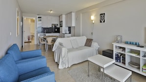 A modern living room with a sofa, a coffee table, and a dining area with chairs. - Apartment in Blankenberge With Sea Views (Blankenberge)