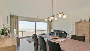 A modern dining area with a large table, chairs, and a view of the sea through a large window. - Flat in Blankenberge With Ocean Views (Blankenberge)