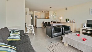 A modern living room with a grey sofa, black leather chairs, a dining table, and a kitchen area in the background. - Flat in Blankenberge With Ocean Views (Blankenberge)