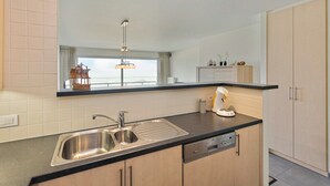 A modern kitchen with a black countertop, stainless steel sink, and wooden cabinets. - Flat in Blankenberge With Ocean Views (Blankenberge)