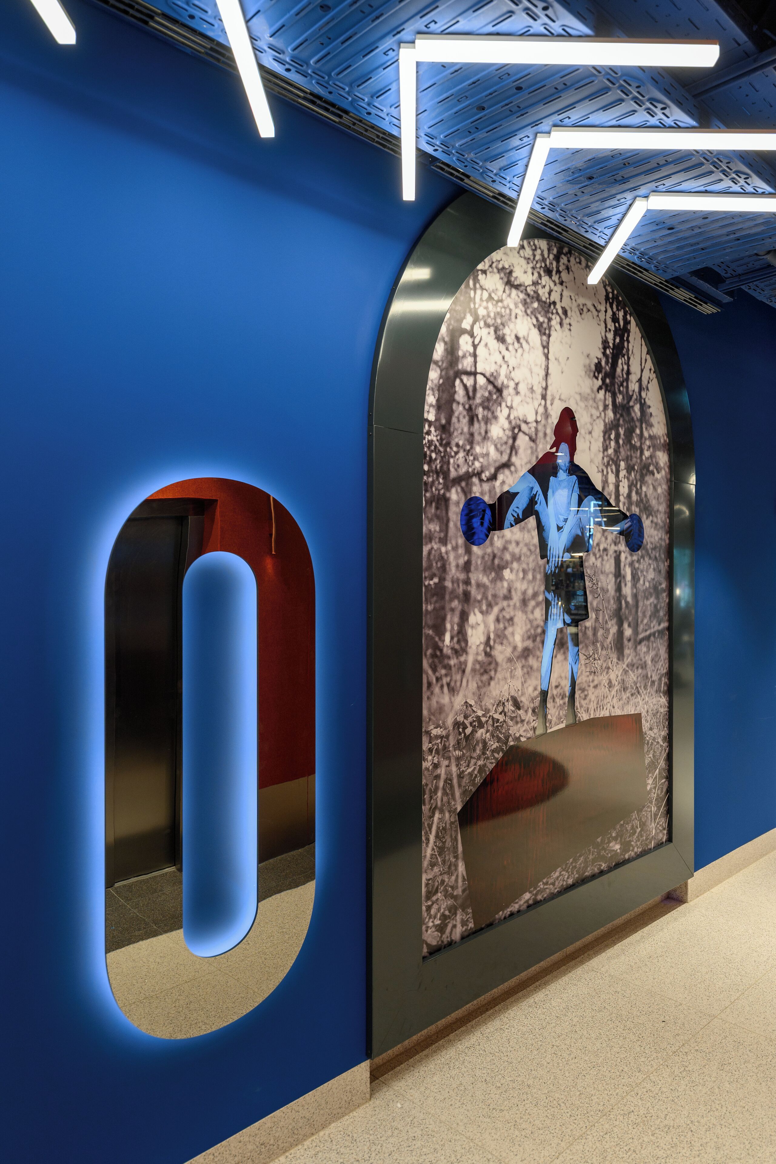 Un interior moderno con una pared azul, un gran ventanal en arco y una pantalla digital que muestra a una persona.