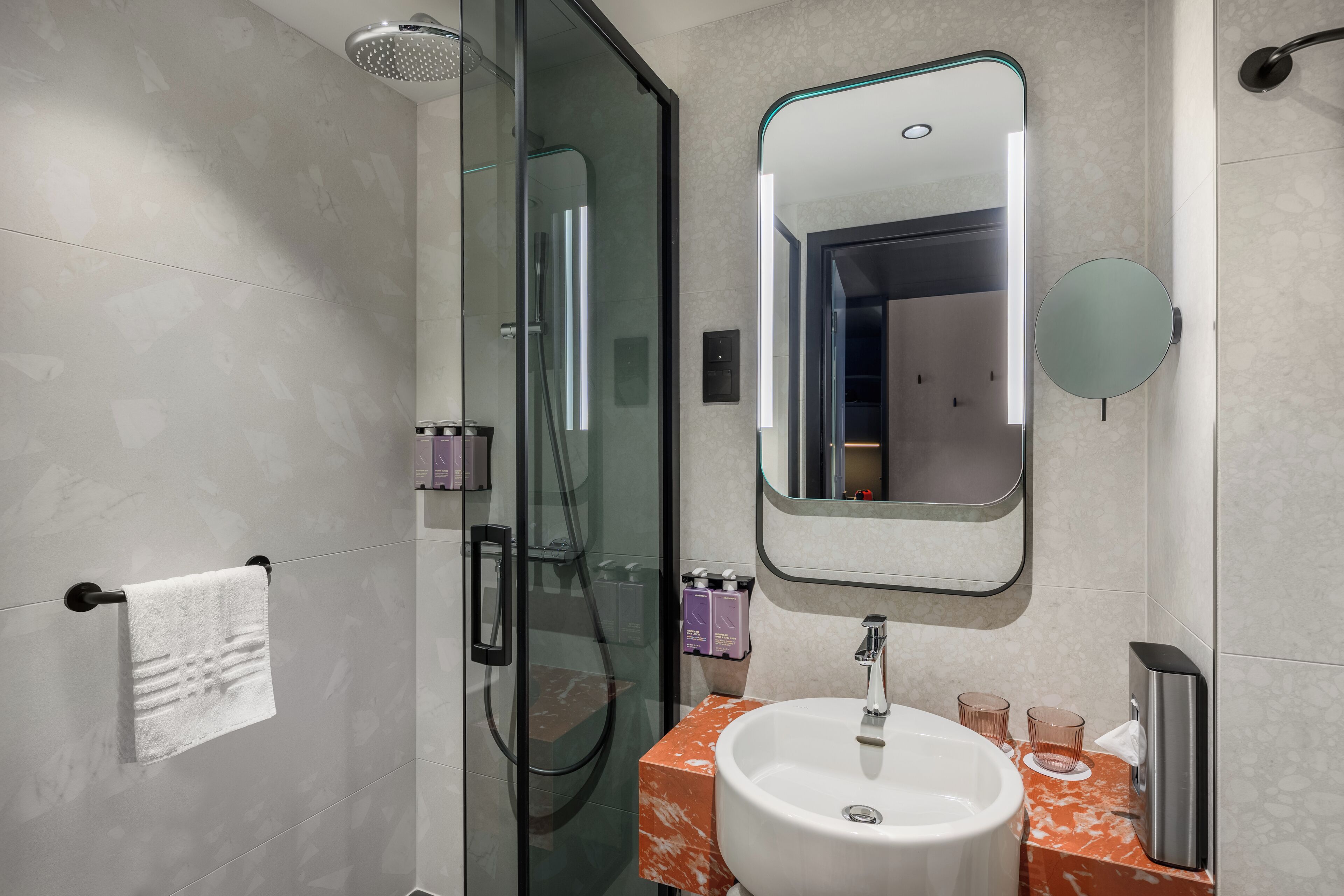 Une salle de bain moderne avec une douche à parois de verre, un lavabo en marbre et un grand miroir.