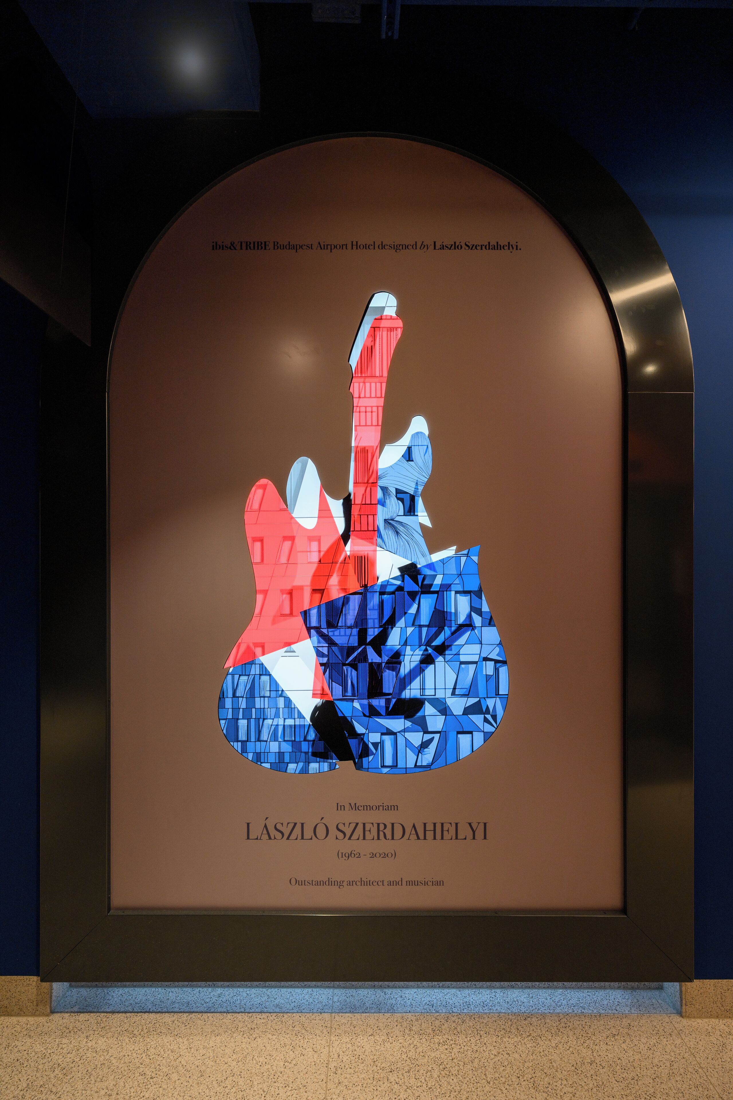 Obra enmarcada de una guitarra con un diseño geométrico, dedicada al arquitecto y músico László Szerdáhelyi, expuesta en un marco oscuro y arqueado.
